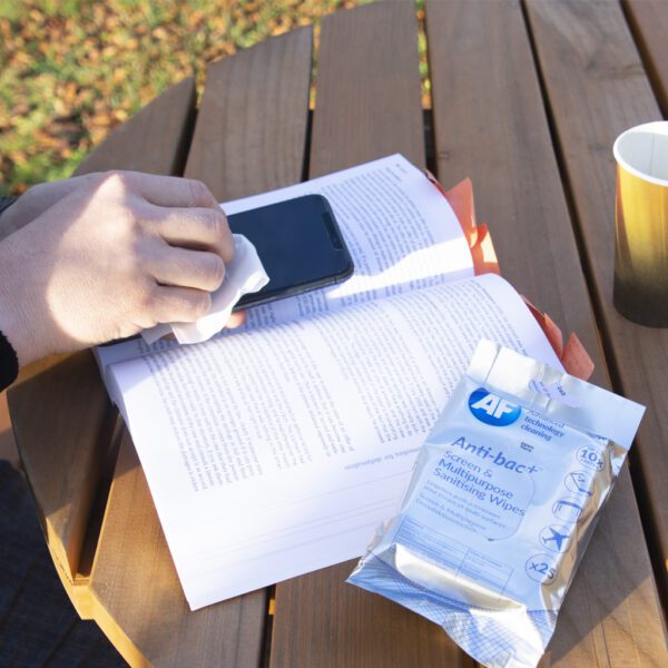A person reading a book on a wooden table and using Anti-bac+ Sanitising Antibacterial Screen & Multipurpose Wipes - x25 ABTW025P.