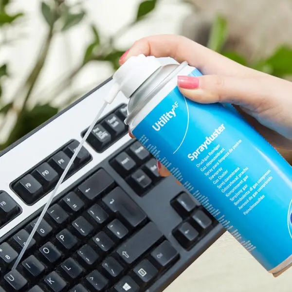 A person spraying a Utility Sprayduster Non-Invertible, Flammable - 400ml ADU400UT on a keyboard.