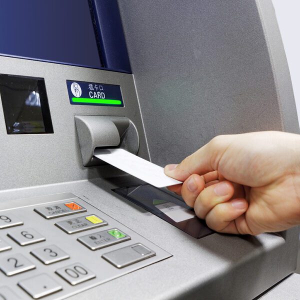 Une personne insérant un Cardclene - Cartes de nettoyage à tête magnétique et contact à puce ATM - x20 CCE020C dans un distributeur automatique.