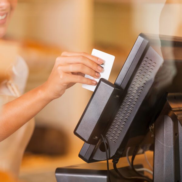 Eine Frau hält eine Cardclene – Magnetkopf-Kartenleser-Reinigungskarten – x20 CCP020 vor einer Registrierkasse.