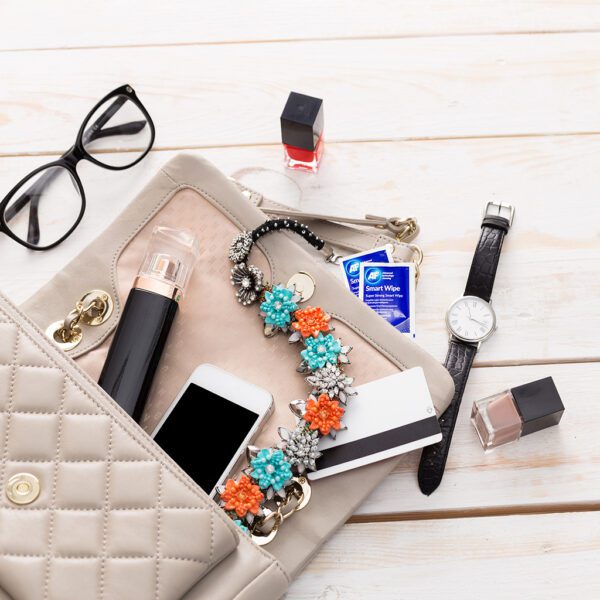 Eine Damenhandtasche mit Smart Wipes – wiederverwendbare Trockenlinsen- und Bildschirmreinigungstücher – x10 SMARTWIPE10 und anderen Gegenständen auf einem Holztisch.