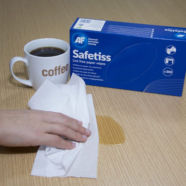 Eine Hand hält eine Tasse Kaffee neben einer Schachtel Safetiss – fusselfreie Papiertücher – x200 STI200.