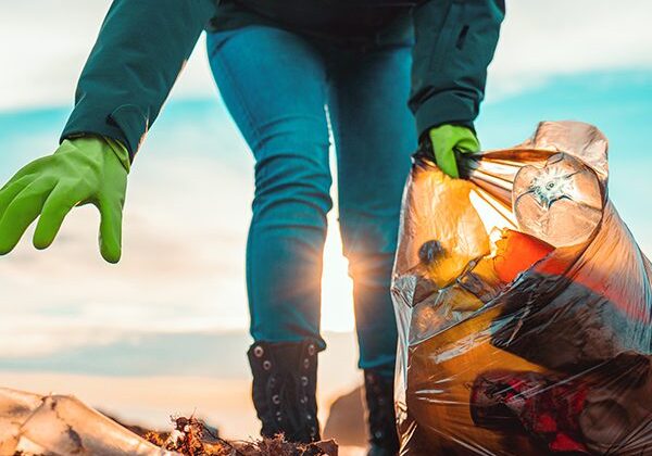 Eine Frau, die Handschuhe trägt, sammelt fleißig Müll am Strand ein, um einen Beitrag zu „5 Ways to Clean Up The Environment“ zu leisten.